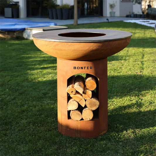 Rust-colored corten steel bonfeu bonbiza xl plancha grill fire pit with circular cooking surface and stacked logs visible