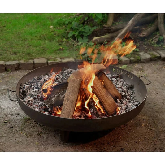 Black metal BonFeu BonBowl Plus corten steel fire pit with handles burning logs and glowing embers inside