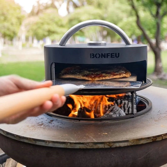 Black BonFeu BonPizza portable wood-fired pizza oven with silver handle and visible flames beneath for outdoor cooking