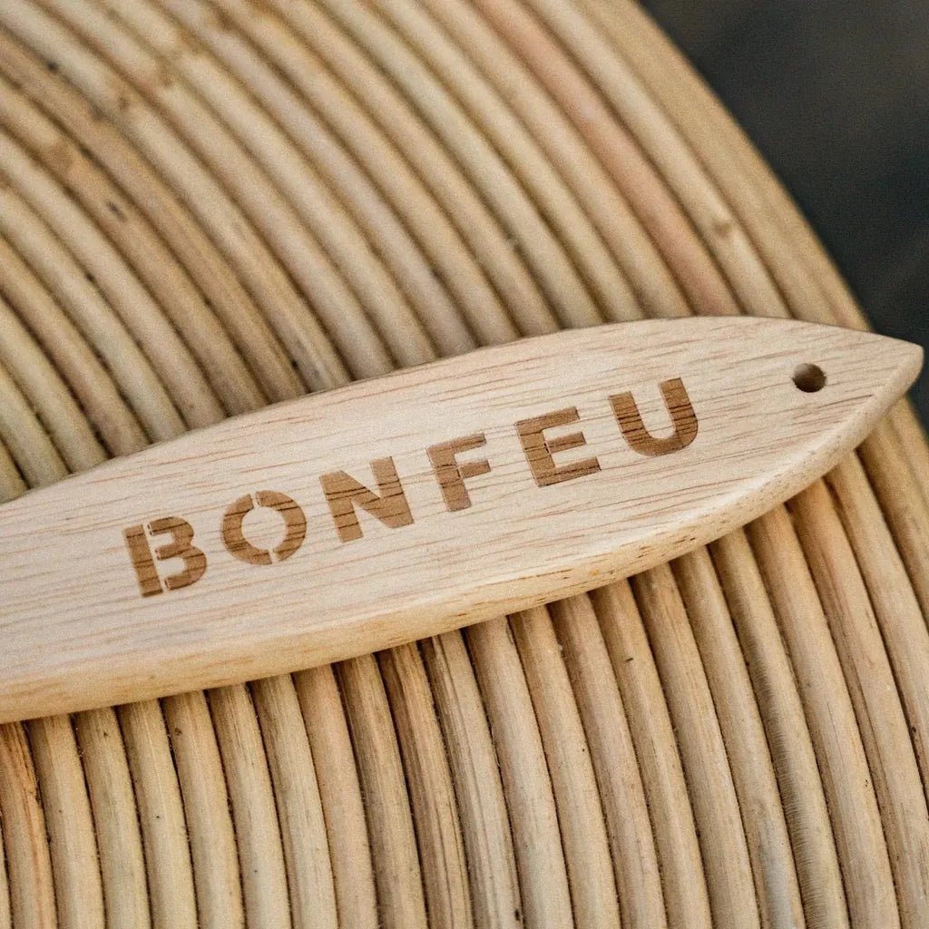 A light-colored wooden bonfeu pizza spatula tag with engraved branding resting on a woven surface