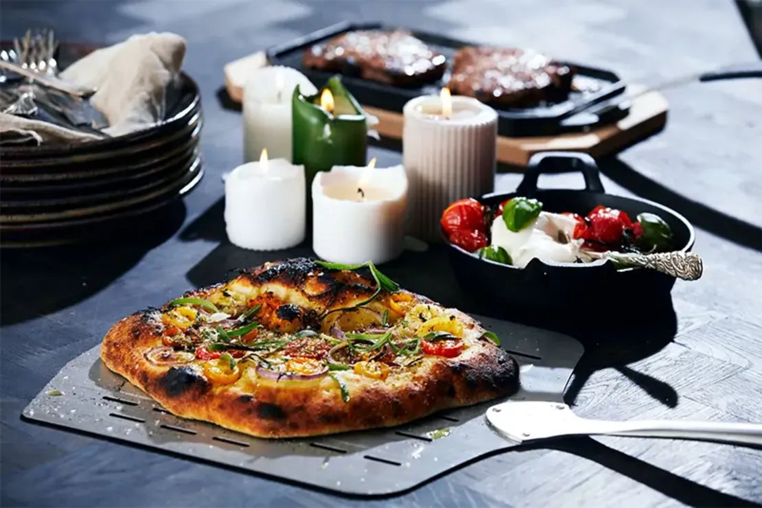 A freshly baked golden-brown pizza with colorful toppings on a metal spatula from Cozze 13 inch premium rotate gas pizza oven