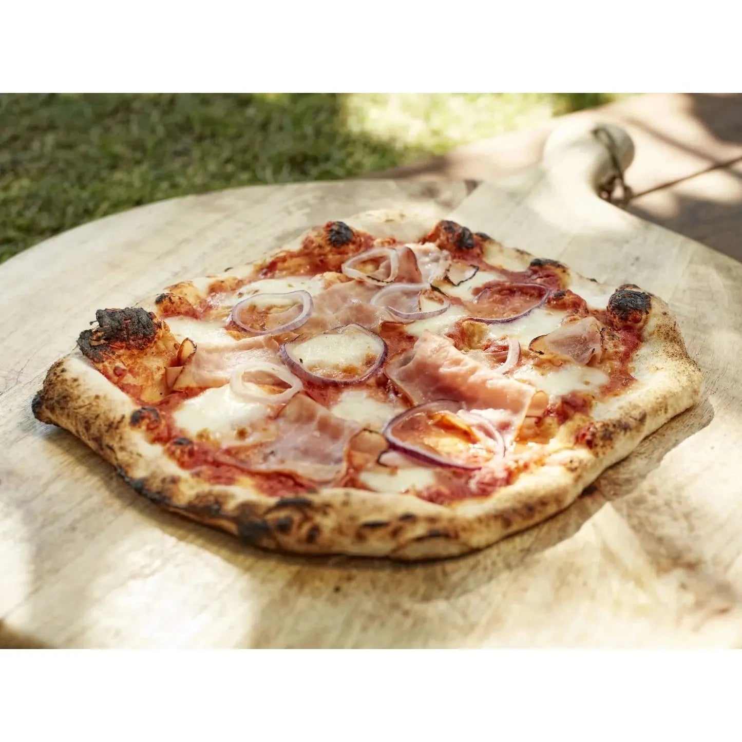 A freshly baked pizza with golden crust, melted white cheese, red onions, and cured ham made in Cozze 17 classic gas oven