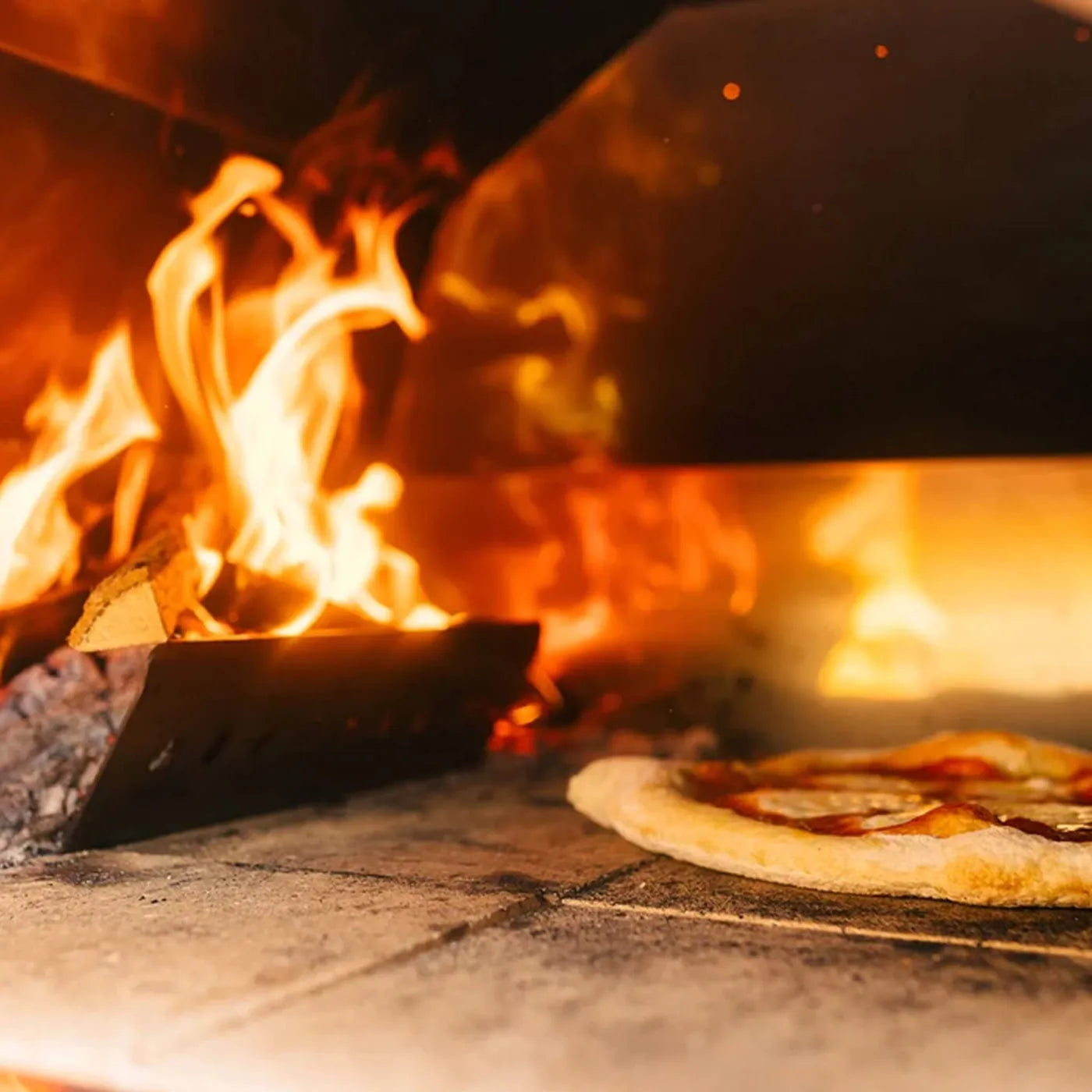 A freshly baked pizza with golden crust beside a red Fontana Mangiafuoco rosso built in wood-fired pizza oven