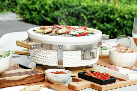 White ceramic kamado grill grllr tokyo shichirin with stainless steel accents wooden handles and grilled meats on mesh surface