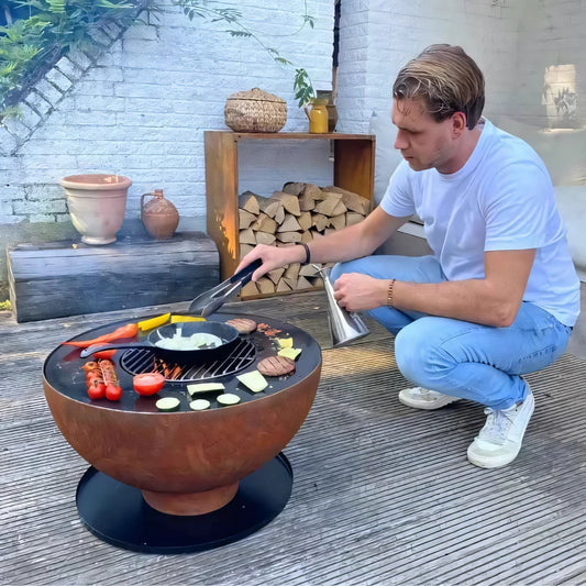 Rust-colored spherical fire pit grill with black base and built-in plancha grilling surface by HEAT Gystad