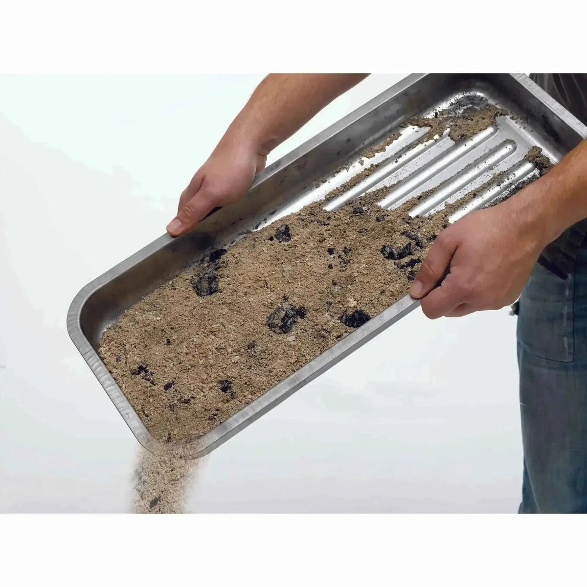 Rectangular stainless steel martinsen charcoal tray with ribbed interior holding sand and dark debris