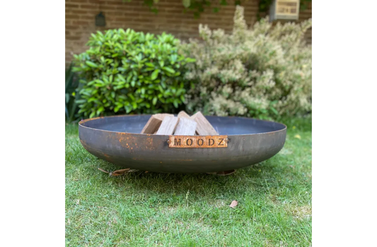 Rustic black metal moodz fire pit with wooden plaque and stacked logs inside corten steel classic fire bowl