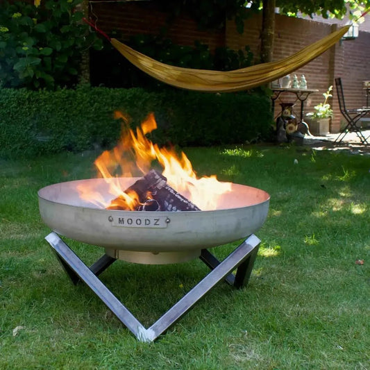 A sleek metallic gray moodz frame garden fire bowl with a modern v-shaped stainless steel stand and engraved rim