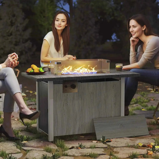 Gray wood-grain outdoor gas fire pit table with clear glass top and glowing flame display by Outsunny