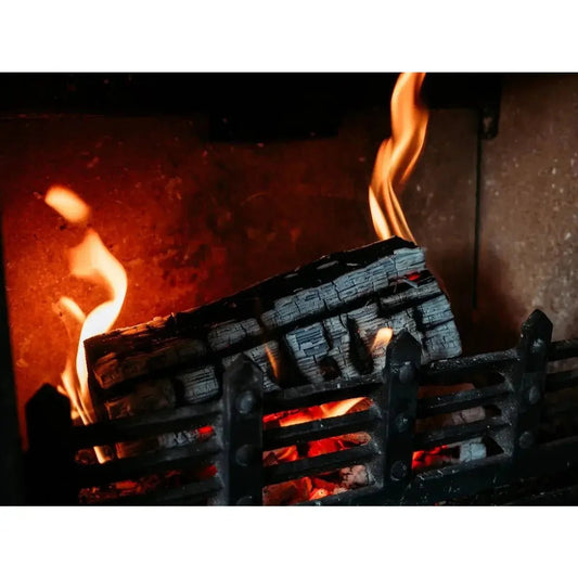 Charcoal-black firewood log burning with orange flames and glowing embers in a fire pit for wood fuel choice