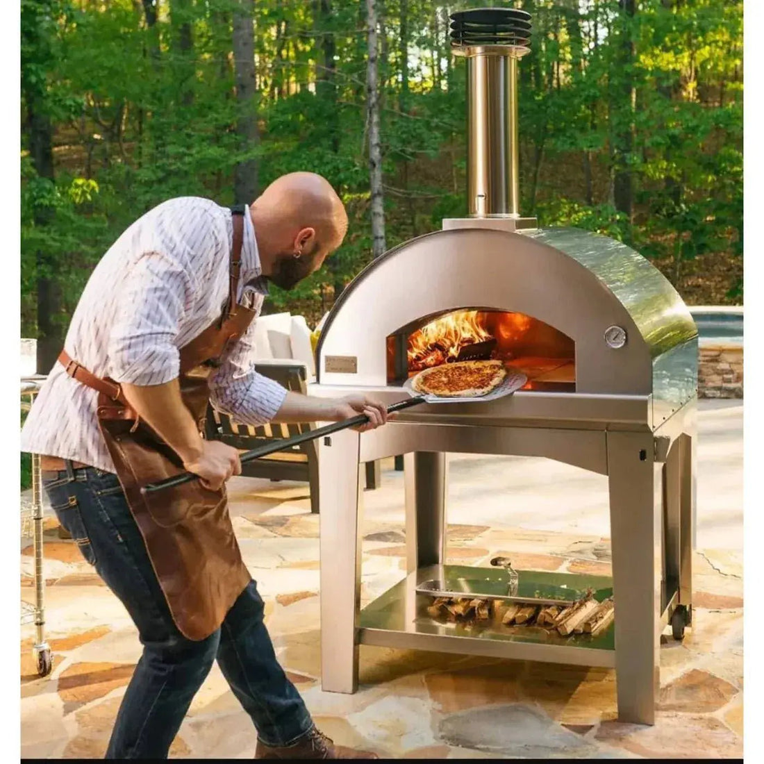Stainless steel outdoor pizza oven with tall chimney and lower shelf holding firewood under £1000