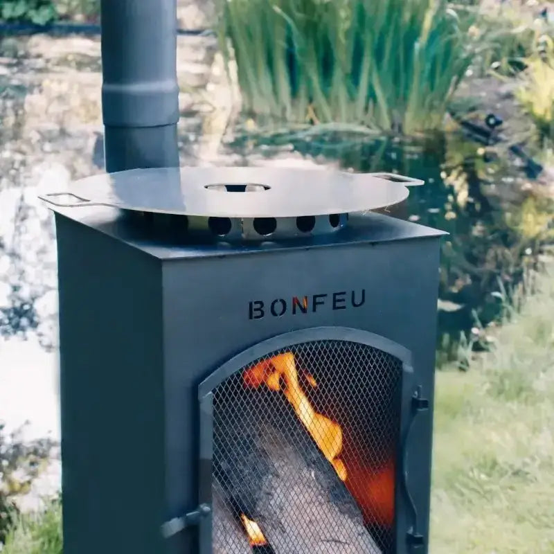 A BonFeu outdoor fireplace with burning logs and cooking plancha on top