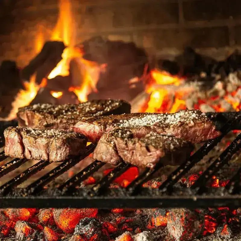 Steaks grilling over embers of a wood or charcoal BBQ