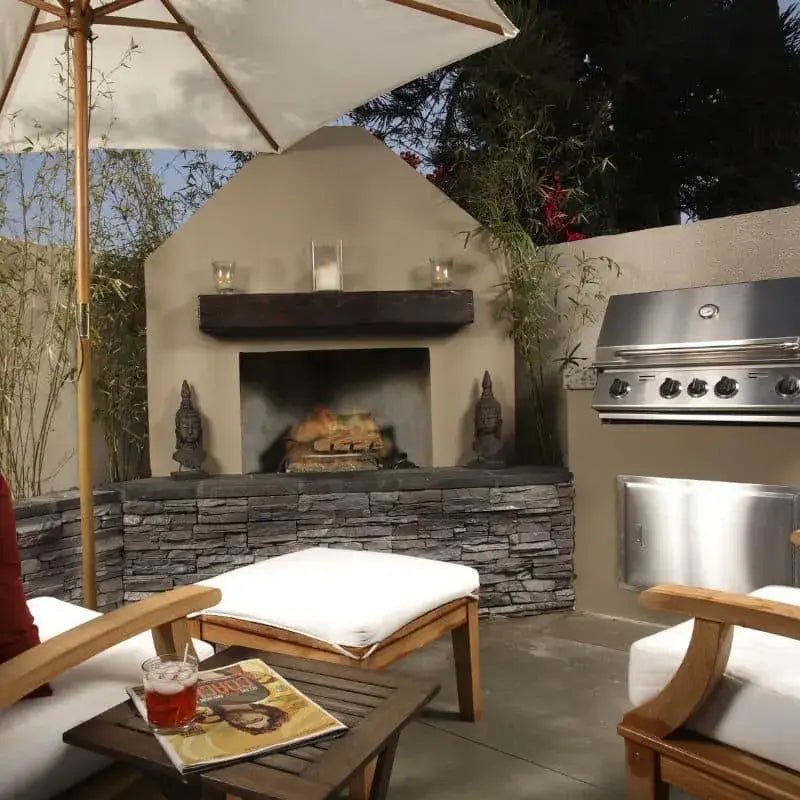An outdoor kitchen with fireplace, BBQ and fridge, in front of outdoor furniture and parasol
