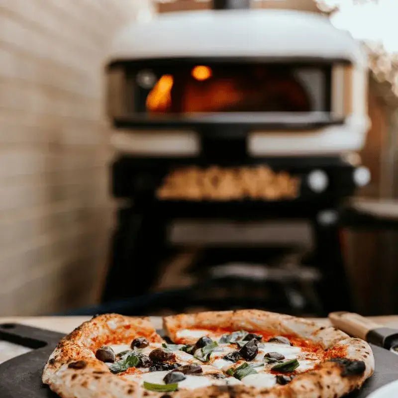 Tabletop wood-fired pizza oven with freshly cooked pizza in foreground