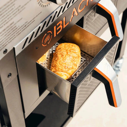 Golden-brown croissant in stainless steel frying basket inside blackstone 28 inch griddle with air fryer outdoors