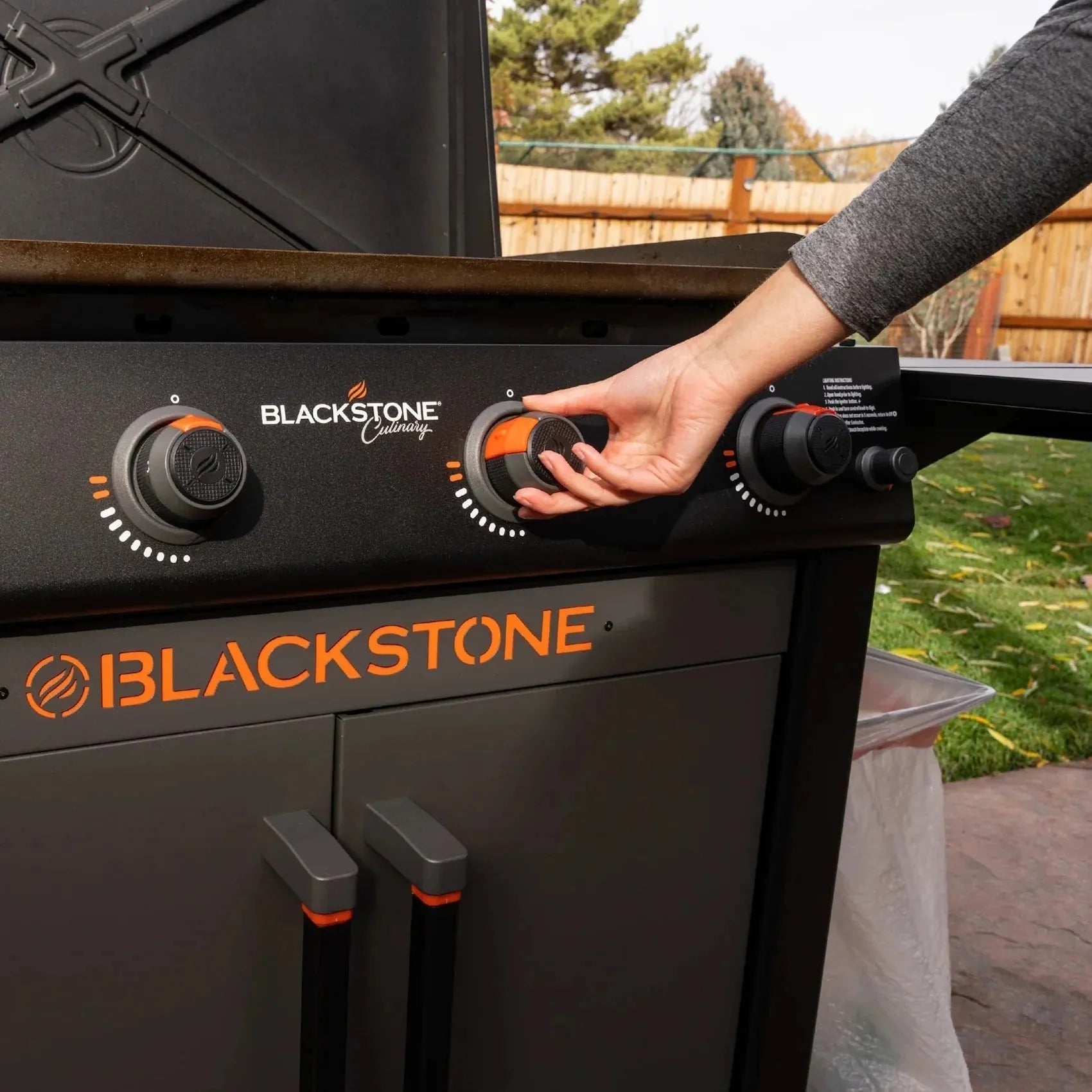 Blackstone culinary 36 inch griddle with cabinet and side table featuring black and orange knobs and stainless steel surface