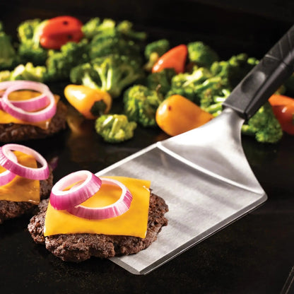 Silver spatula with black textured handle lifting cheeseburger patty with cheddar and onion in blackstone smash burger kit
