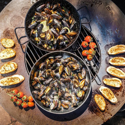 Black speckled cast iron pans filled with steaming mussels on a bonfeu bonbiza open plancha grill fire pit