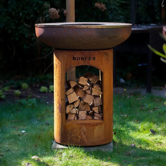 Rustic copper-toned bonfeu bonbiza open plancha grill and fire pit with cylindrical wooden base holding stacked logs