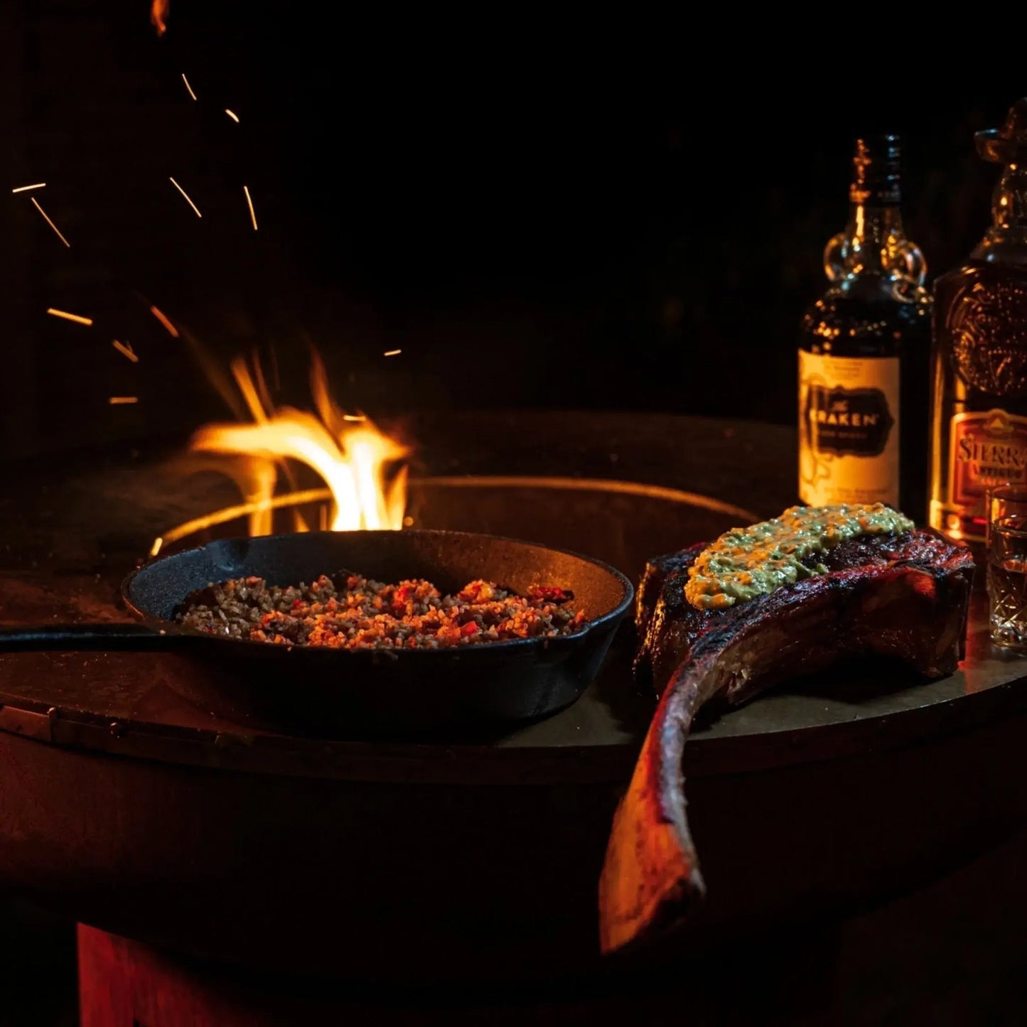 Succulent ribeye steak with herb butter beside a cast iron skillet of seasoned meat on a bonfeu bonbiza open plancha grill