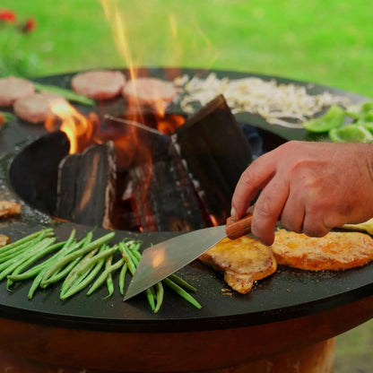 Bonfeu bonbiza black circular fire pit grill with wooden handle spatula and burning charred wood logs inside