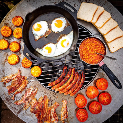 Black cast iron skillet with three sunny side up eggs cooking on bonfeu bonbiza plancha grill fire pit in black steel
