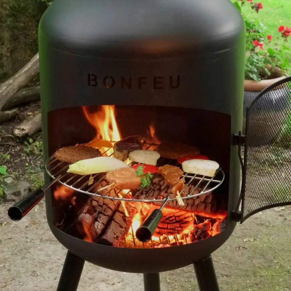 Black bonfeu bonbono large outdoor fireplace chiminea grill with round metal grate cooking meats and vegetables over embers