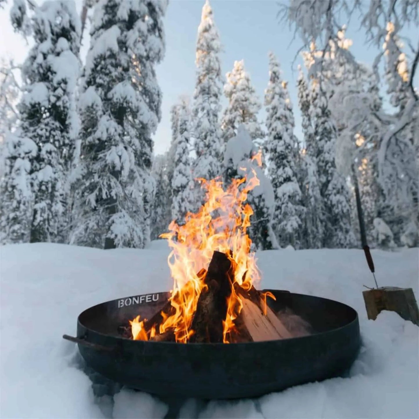 Black metal bonfeu bonbowl plus corten steel fire pit with flames burning surrounded by snow-covered trees