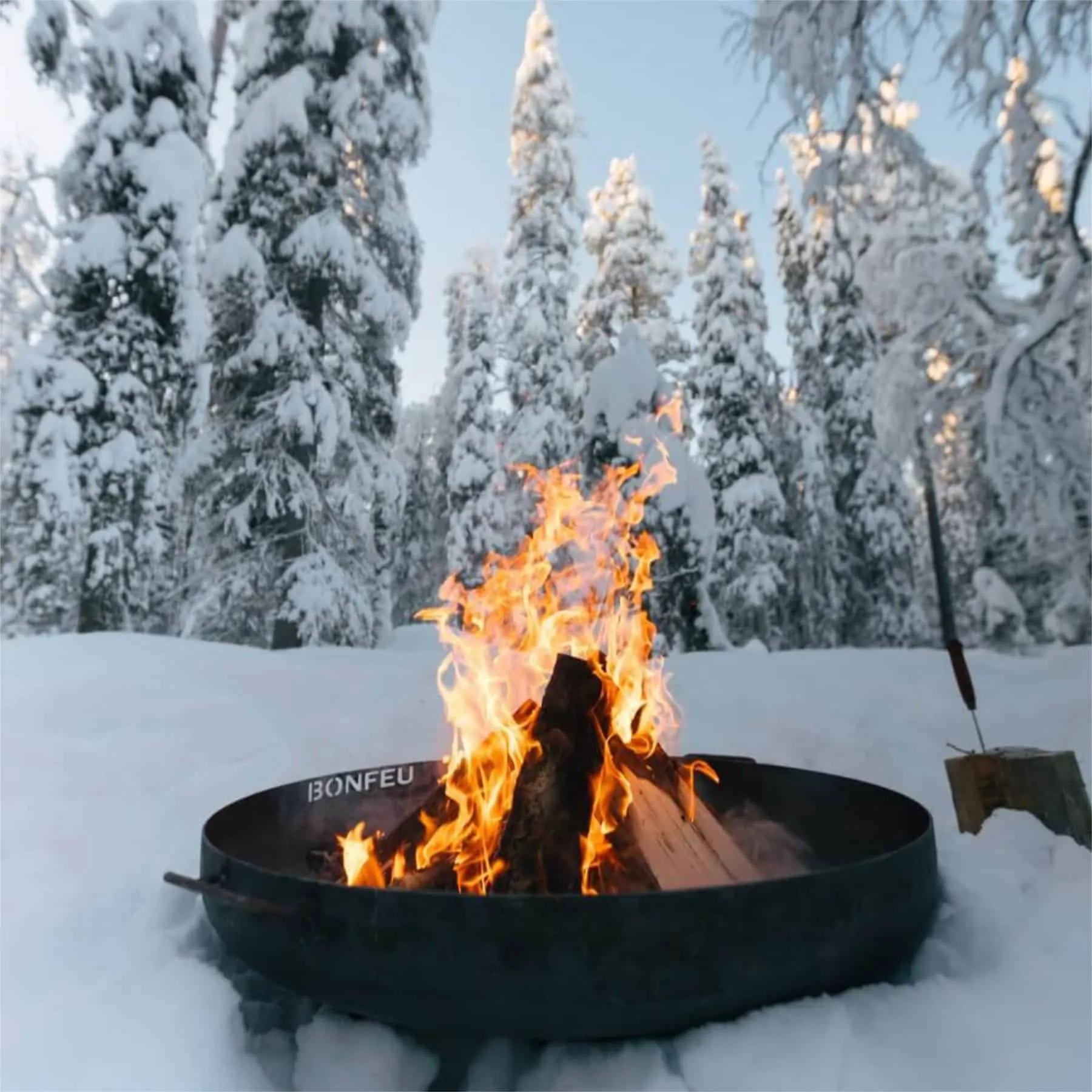 Black metal bonfeu bonbowl plus corten steel fire pit with flames burning surrounded by snow-covered trees