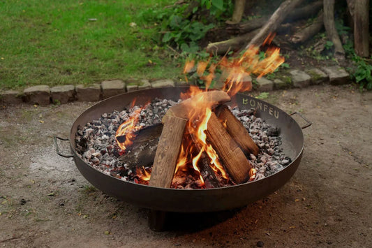 Black metal bonfeu bonbowl plus corten steel fire bowl filled with burning logs and glowing embers