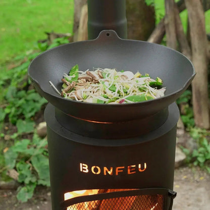 Black cast iron wok with stir-fried vegetables on bonfeu bongiano sp outdoor fireplace in black and corten steel