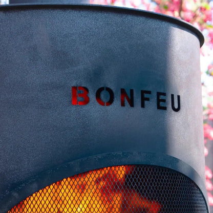 Black matte-finished bonfeu bonton large outdoor fireplace in steel with glowing orange fire visible through mesh screen