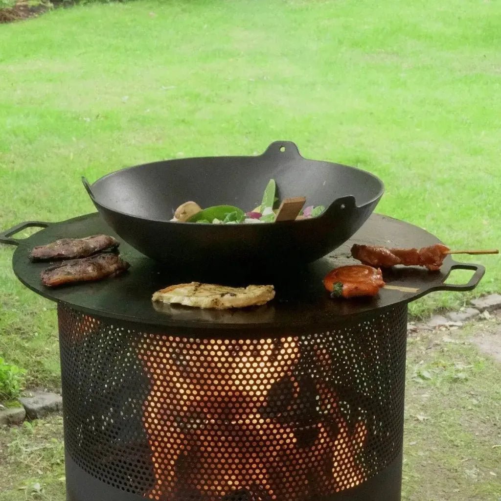 Black cast iron wok resting on a perforated metal bonfeu bonves 45 fire pit with glowing embers visible through holes