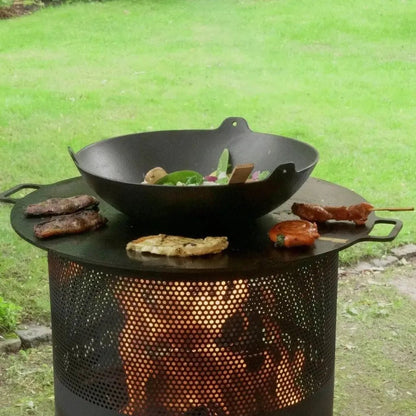 Black cast iron wok resting on a perforated metal bonfeu bonves 45 fire pit with glowing embers visible through holes