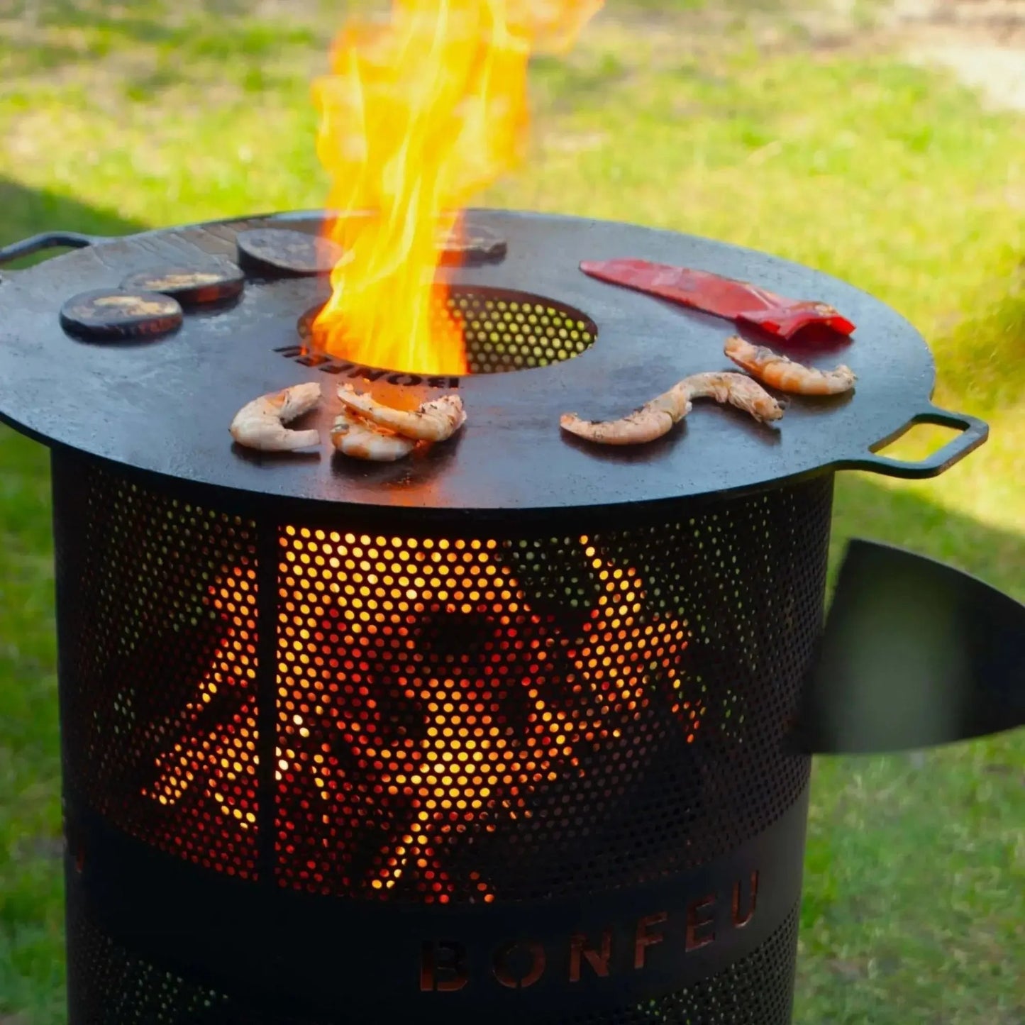 Black perforated metal grill with flame and shrimp cooking on bonfeu plancha for bonfeu outdoor fireplaces