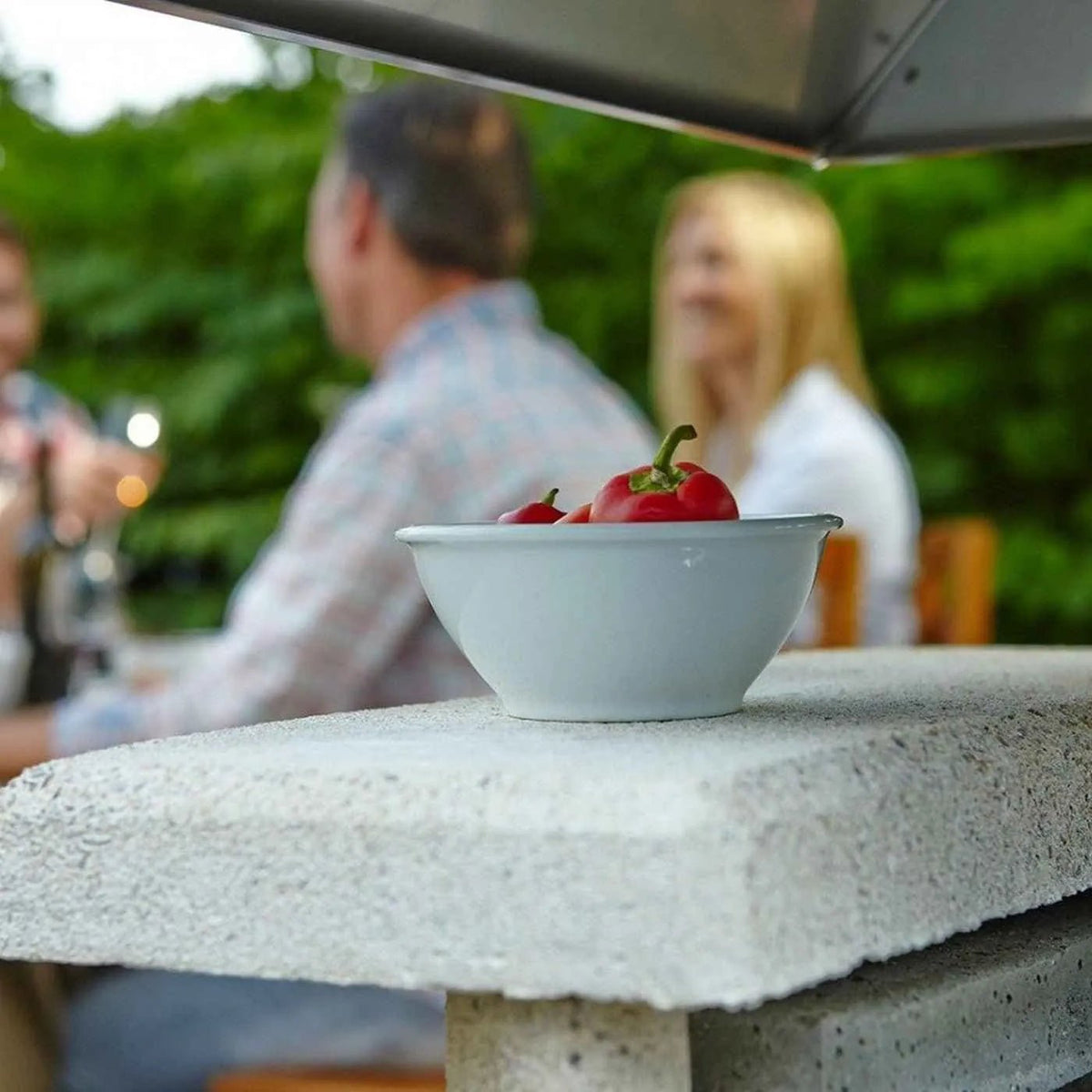 A white ceramic bowl holding red peppers displayed near the buschbeck zurich masonry barbecue in white masonry