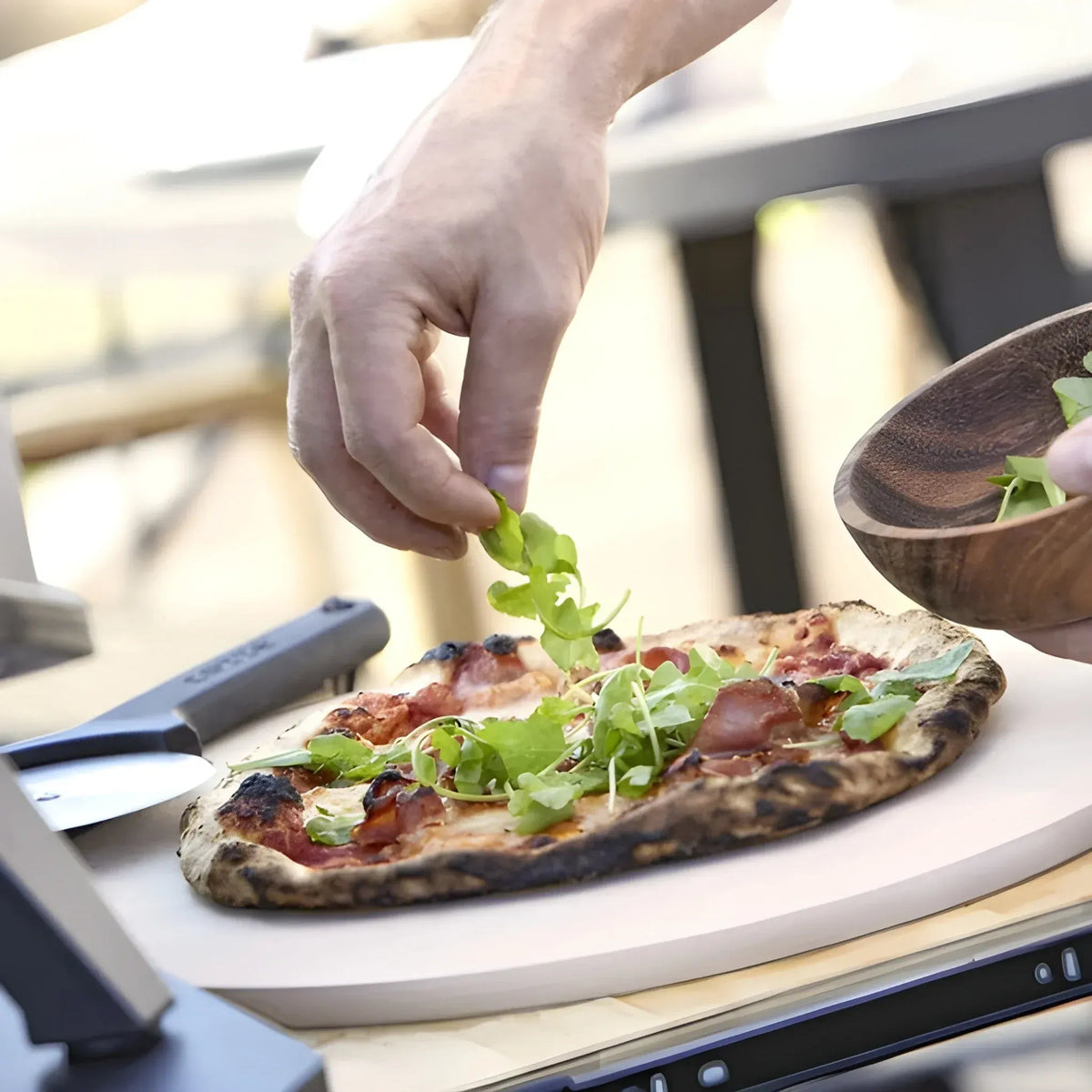 A freshly baked pizza with charred crust, melted cheese, bacon, and arugula in a Cozze 13 inch electric pizza oven premium rotate