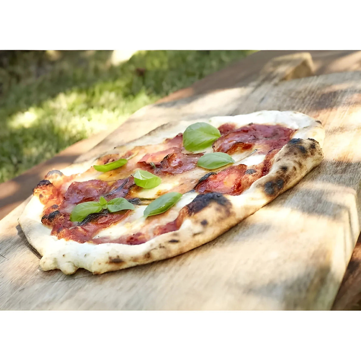 A freshly baked pepperoni pizza with charred edges and basil on a rustic board cooked in Cozze 17 inch electric pizza oven premium rotate