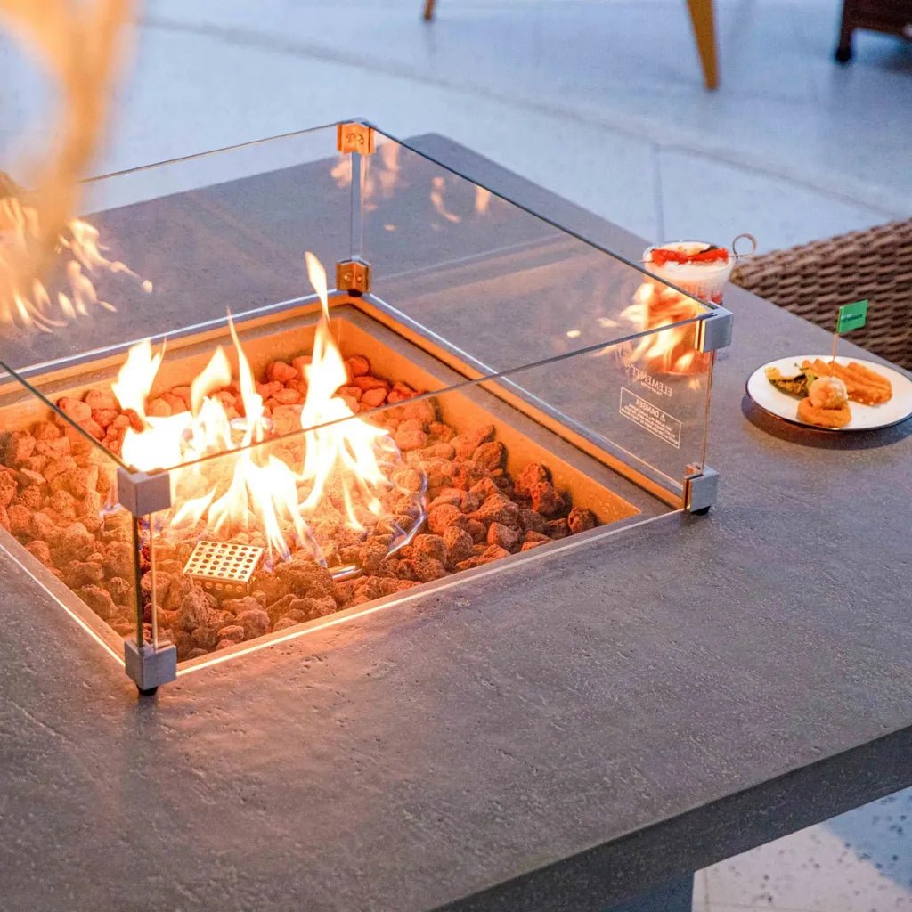 Elementi birmingham dining fire table with square glass enclosure glowing orange flames and dark brown lava rocks