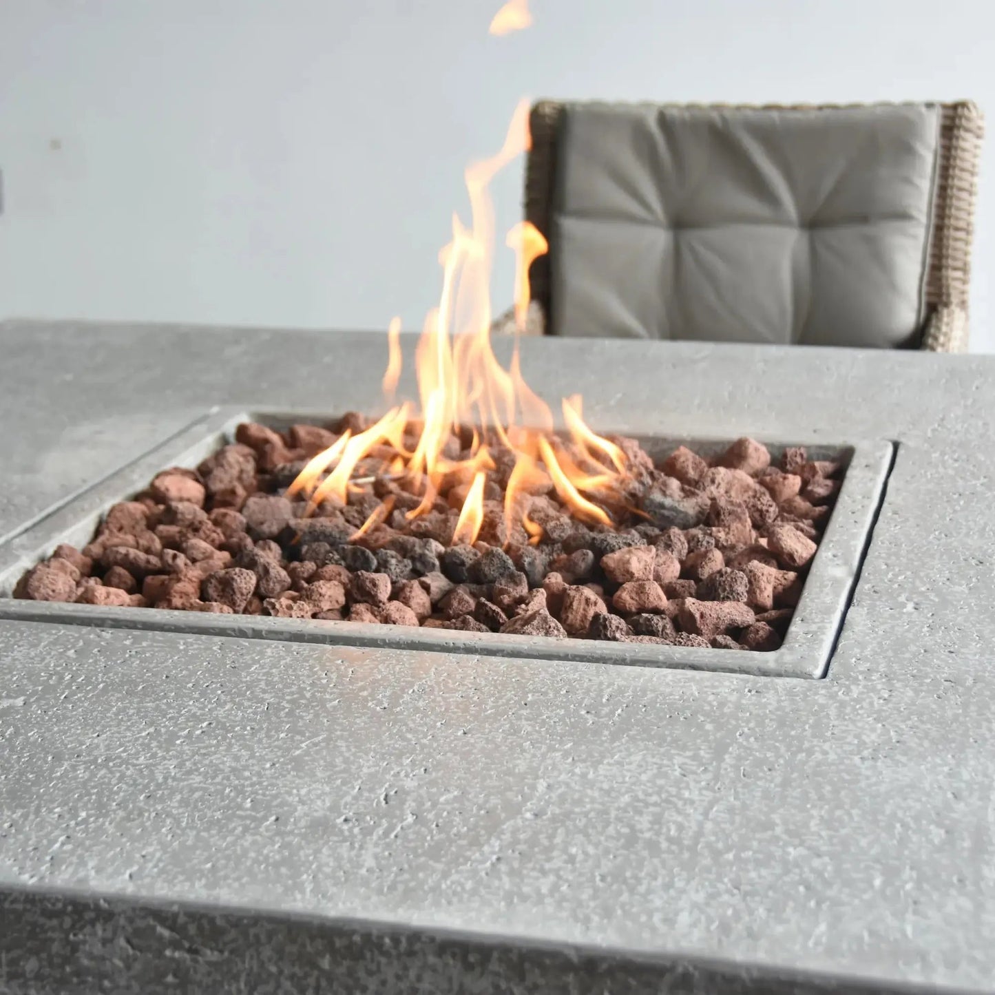 A modern gray concrete Elementi Birmingham dining fire table with square lava rock inset and flickering flames