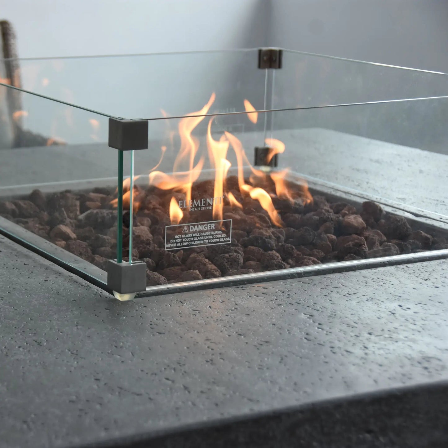 Elementi Birmingham dining fire table with square glass enclosure dark volcanic rock base and black metal frame