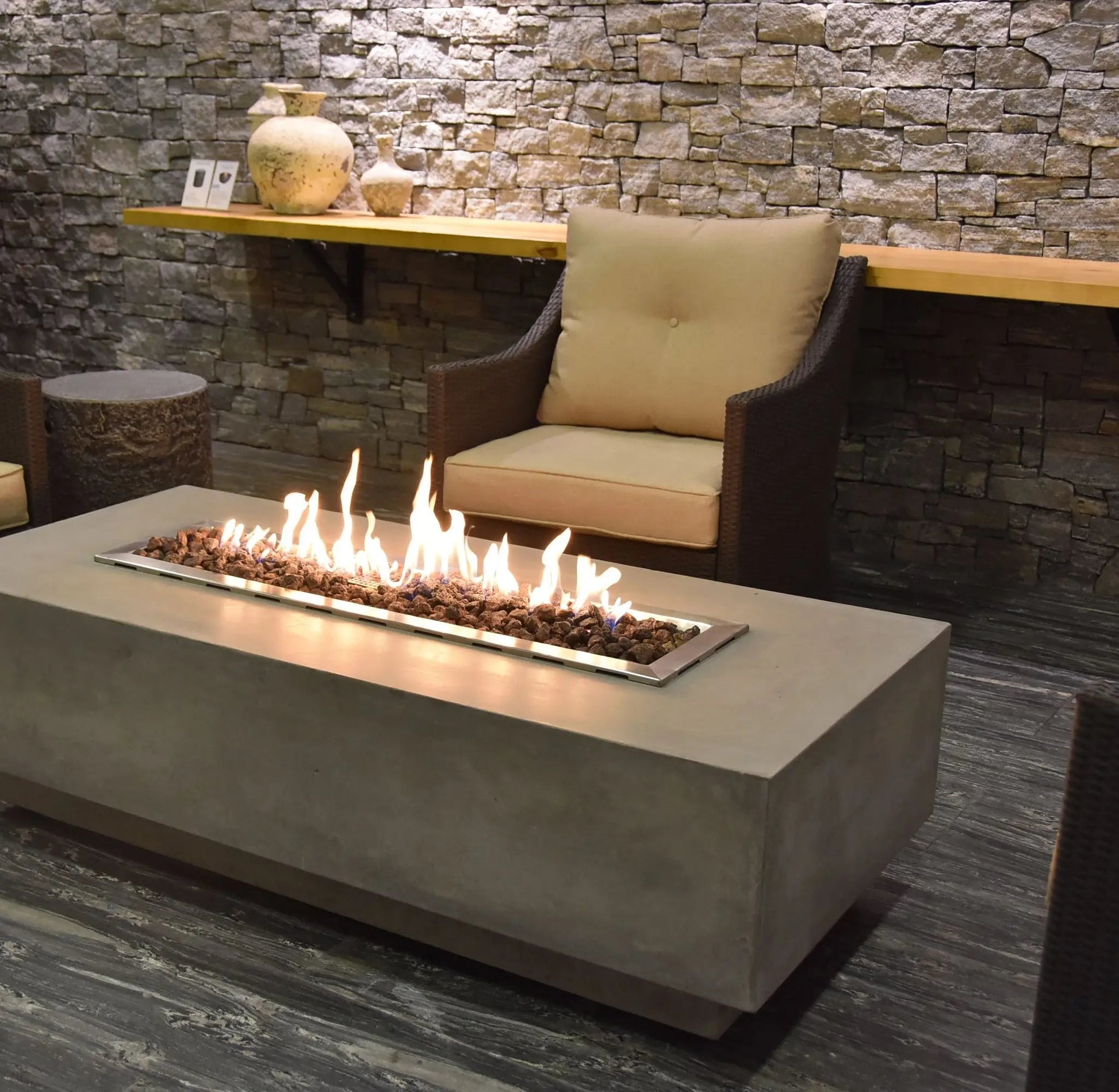 Elementi Granville fire table in concrete with a rectangular metal frame holding glowing embers and flickering flames
