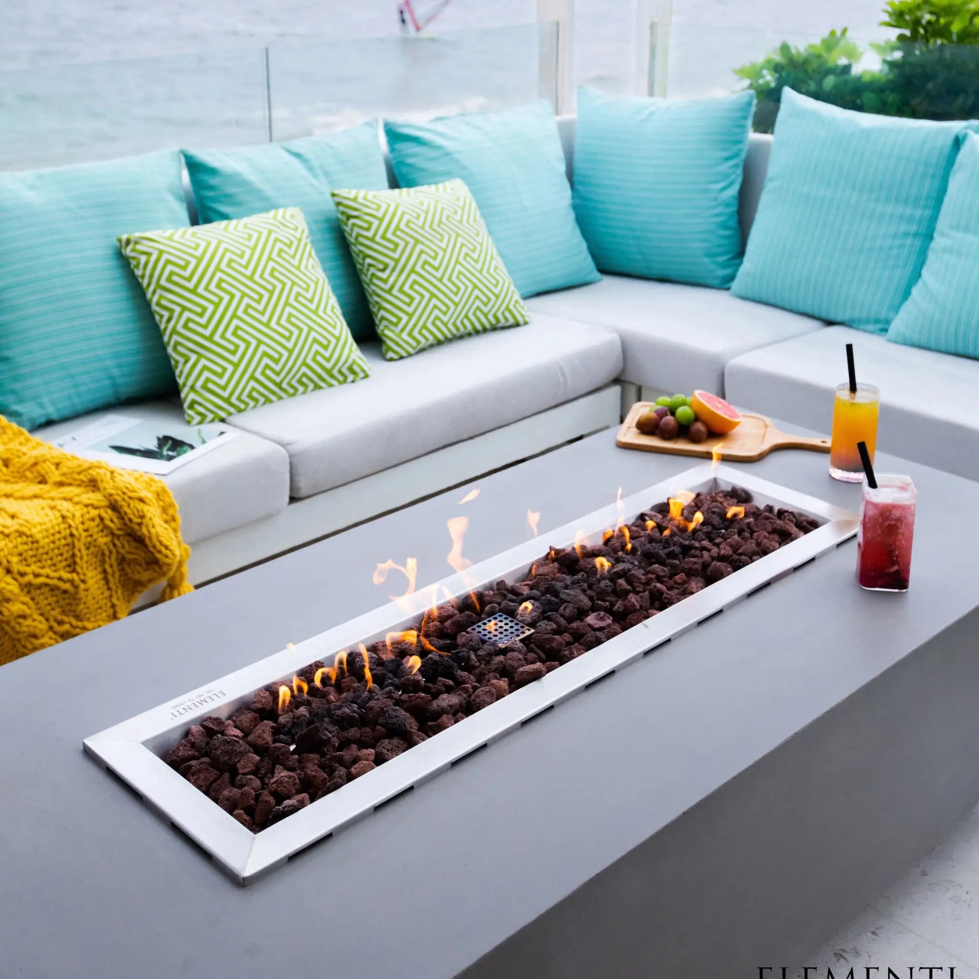 Elementi Granville fire table 13.2 kW rectangular white fire pit with dark brown lava rocks and flickering flames inside
