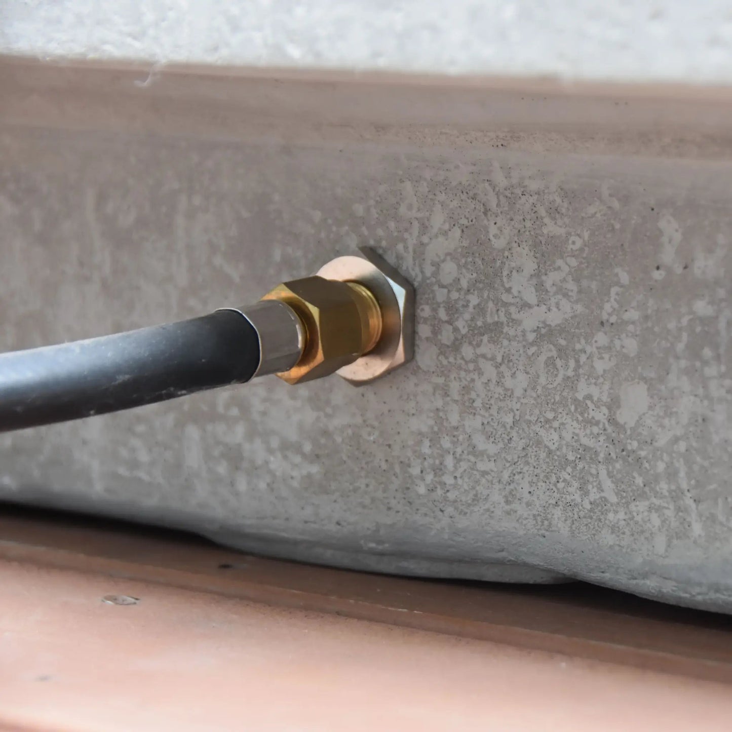 A brass hexagonal pipe fitting securing a black hose to concrete on the elementos hampton fire table 13.2 kw