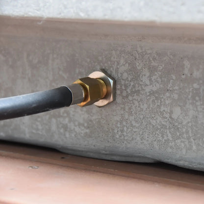 A brass hexagonal pipe fitting securing a black hose to concrete on the elementos hampton fire table 13.2 kw