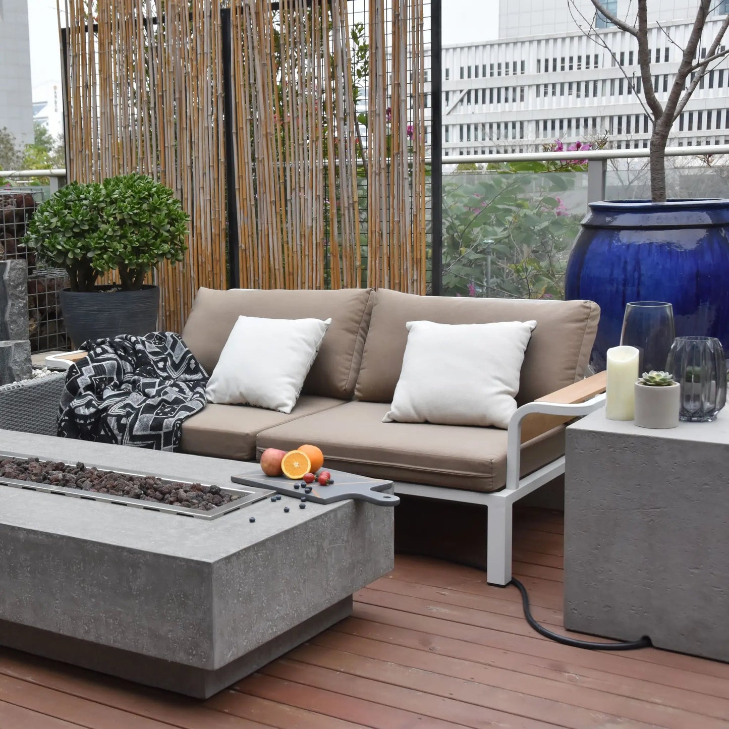Beige outdoor sofa with white pillows and black and white throw blanket paired with elementi hampton fire table 13.2 kw