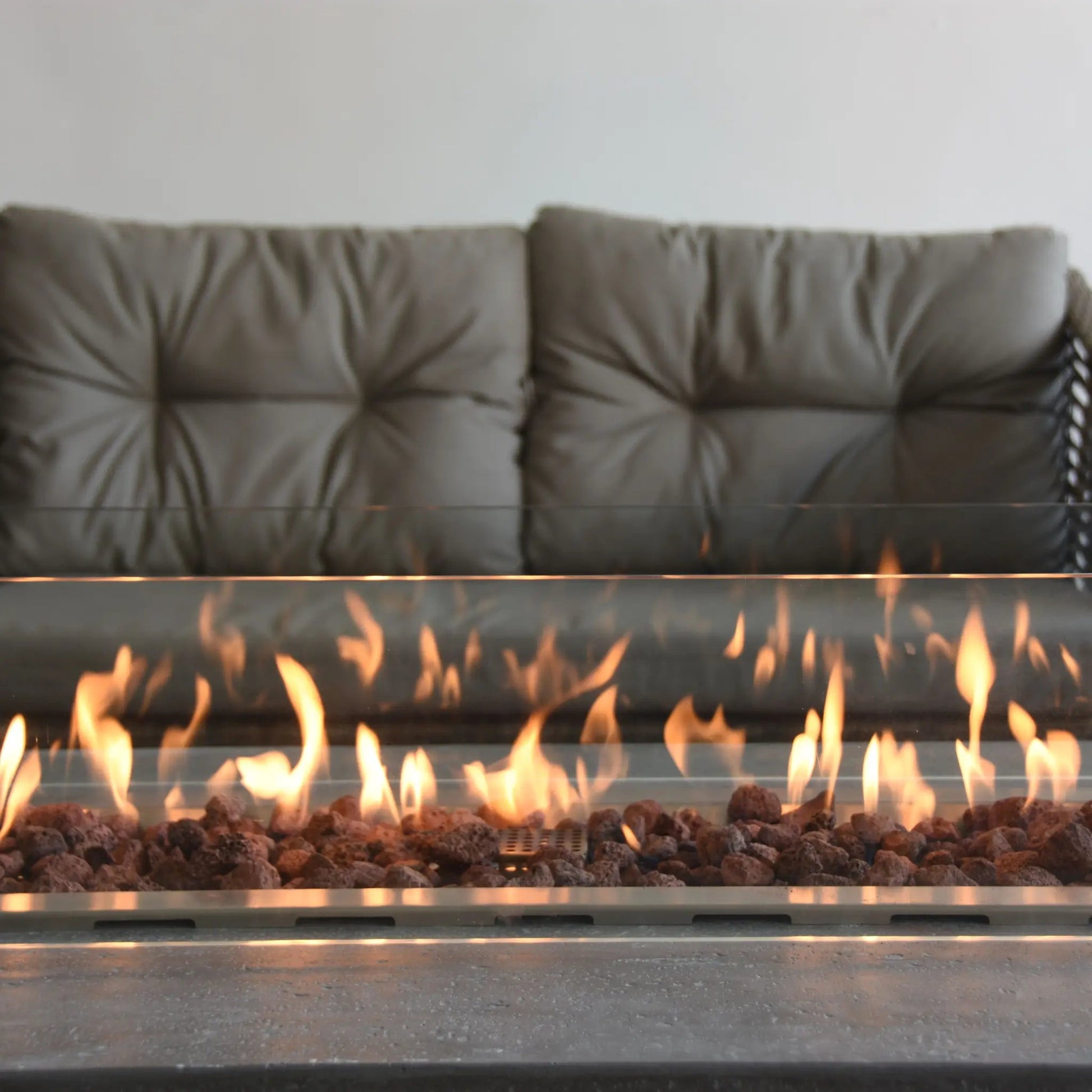 Elementi Kingsale fire table modern gas fireplace with flickering orange flames over reddish-brown lava rocks and metallic rim