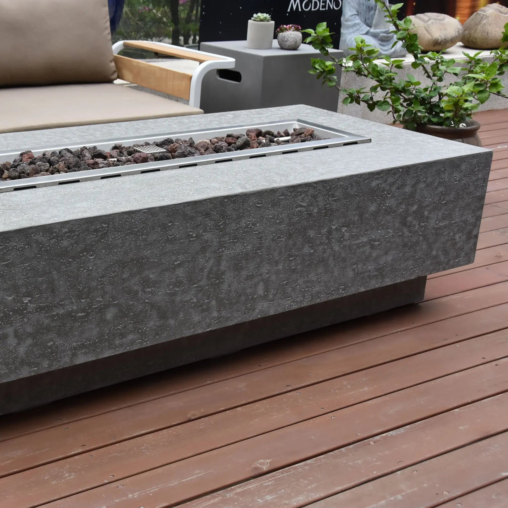 Elementi Kingsale fire table with modern gray concrete body and rectangular metal insert holding dark lava rocks