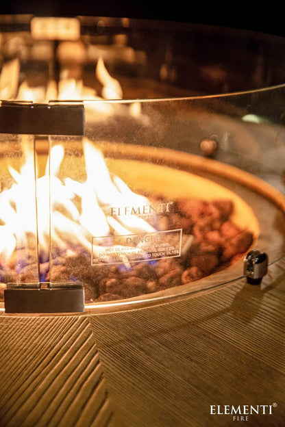 Elementi Lafite barrel bar fire table with clear glass enclosure and reddish-brown lava rocks inside fire pit